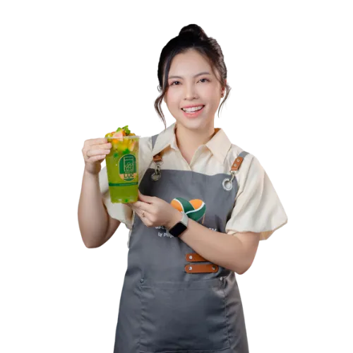 Giảng viên Ly Phạm trong tạp dề Saly Academy, cầm một ly nước ép trái cây